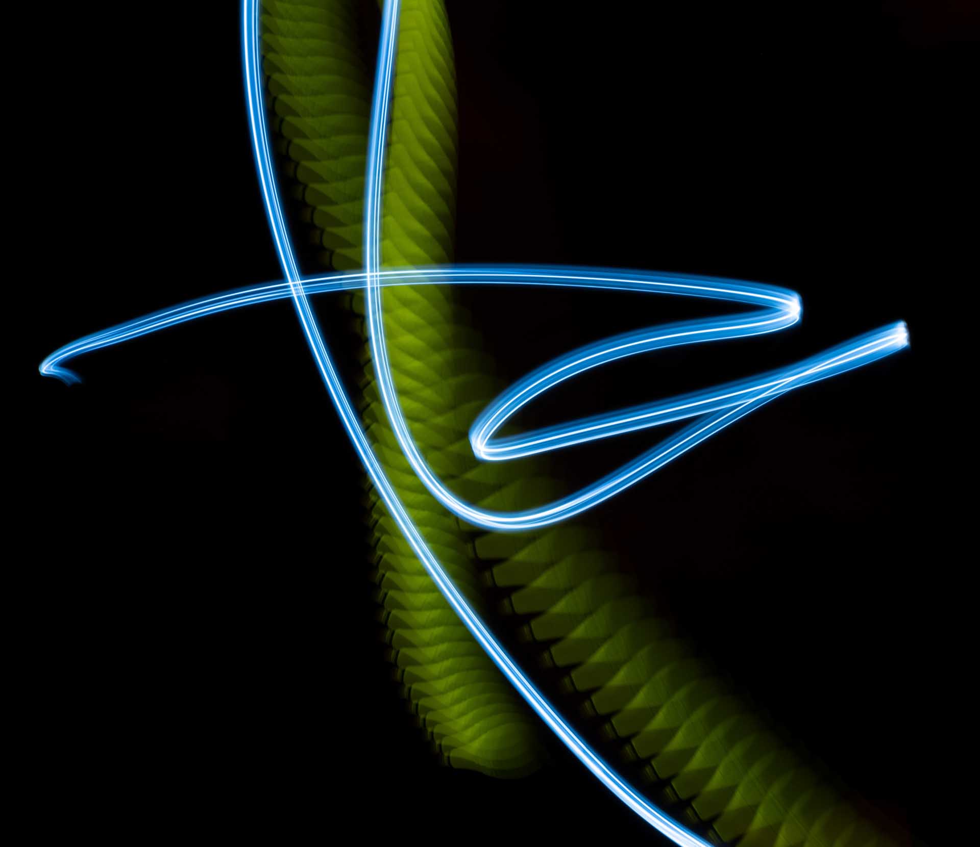 Abstract light painting with blue neon curved lines and a yellow-green textured trail on a black background.