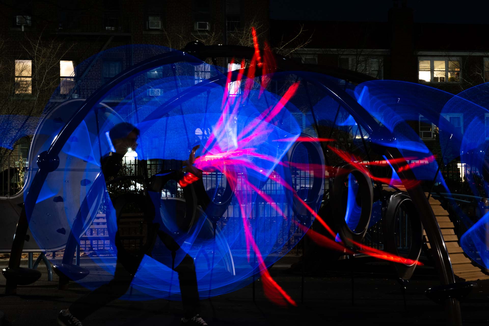 Silhouette of a person creating blue and red light trails at night in an outdoor playground.