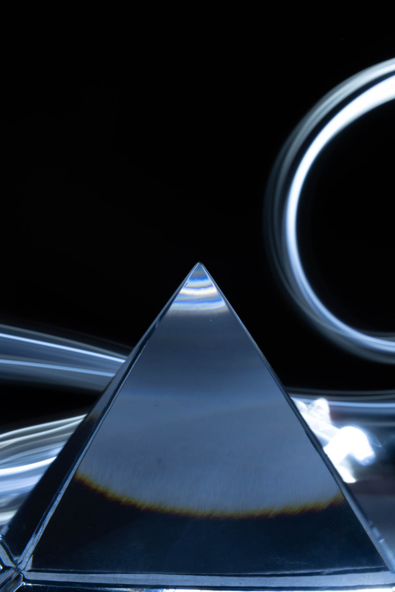 Glass pyramid prism with light streaks and circular glow on black background.