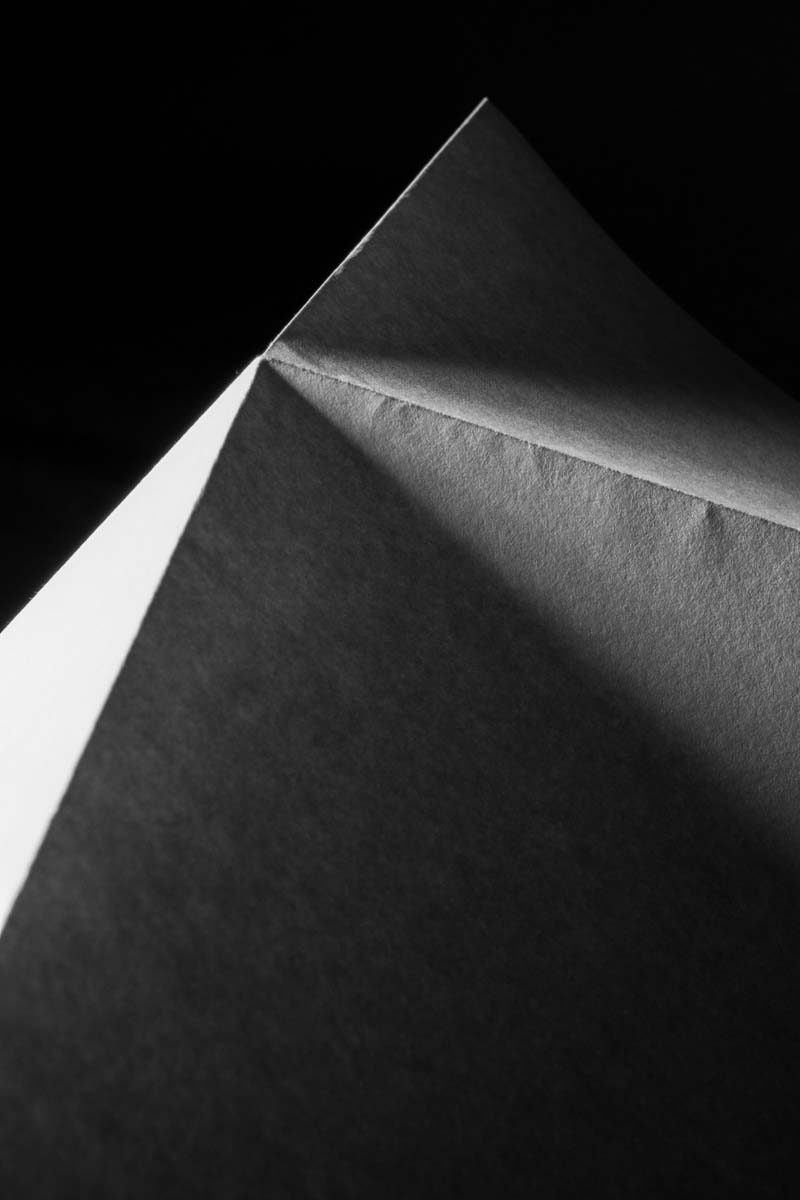 Close-up black and white photo of a paper corner with sharp light and shadow contrast.