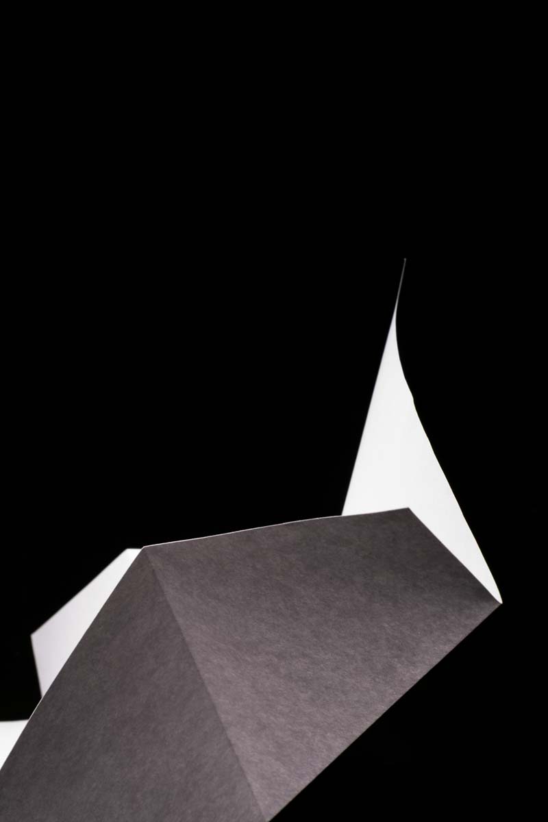 Close-up of a black and white folded paper forming sharp abstract shapes against a black background.