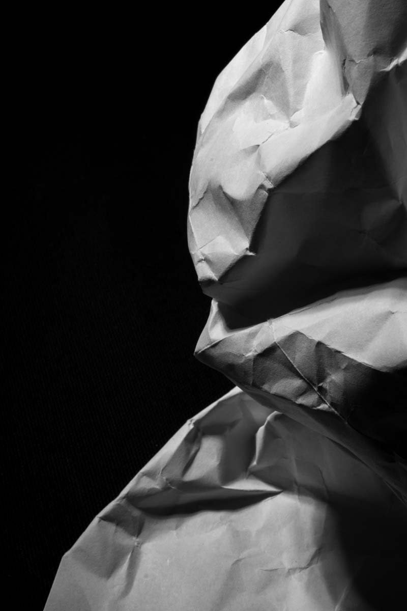 Close-up of crumpled white paper with textured folds against a black background.