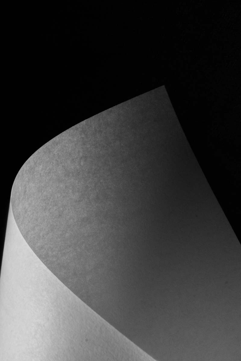 Close-up of a curled white paper sheet with visible texture against a black background.