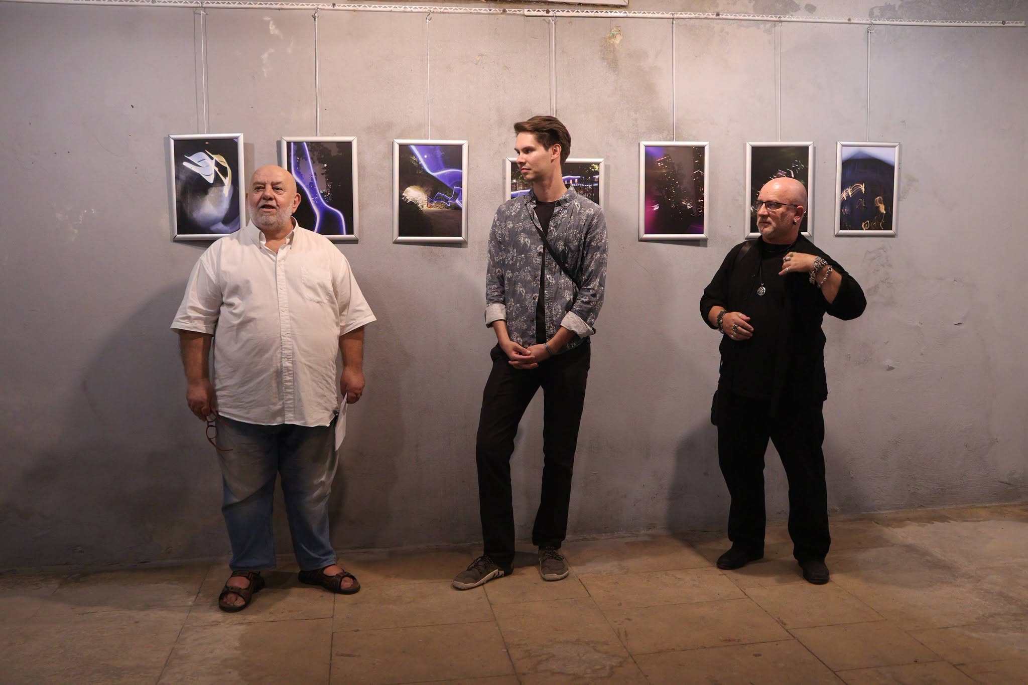 Three people standing in front of a series of photography art works.