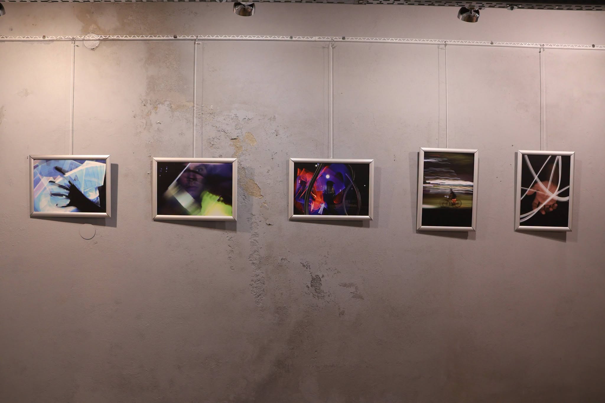 A series of five light-painting photographs hanging on a wall.