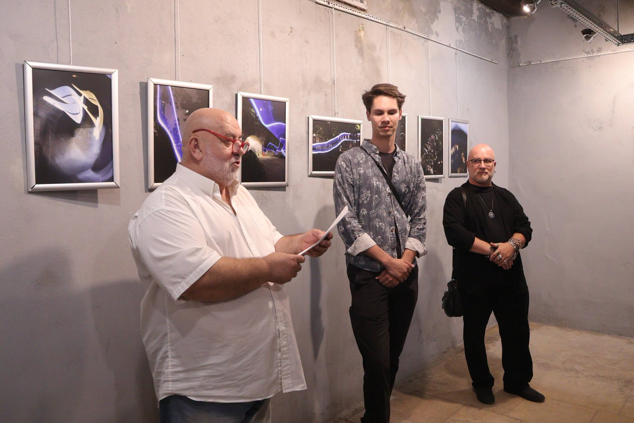 Three people standing in front of a series of light painting photographs. One person presents the series.