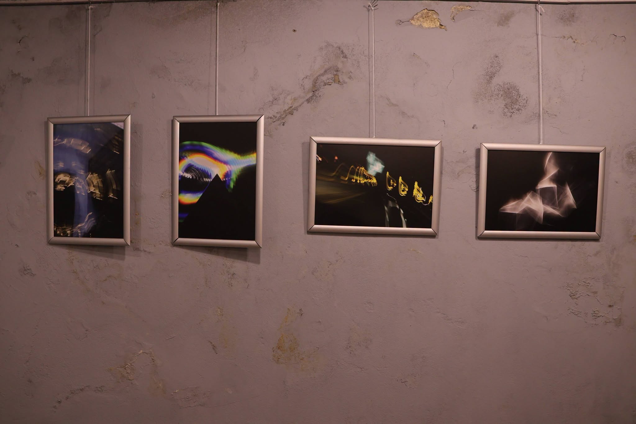 A series of four light-painting photographs hanging on a wall.