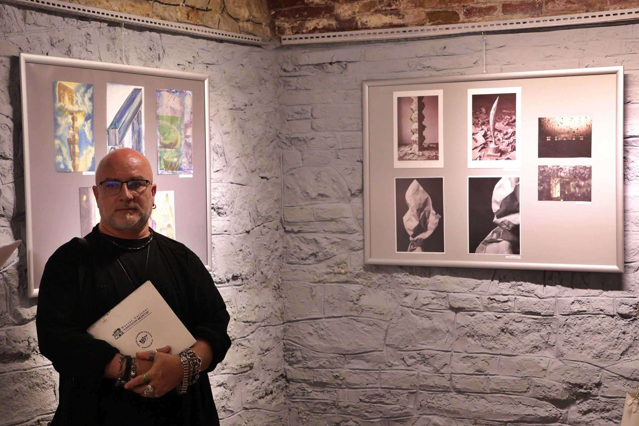 One man stands in front of artwork on the wall at a group mail art exhibition.