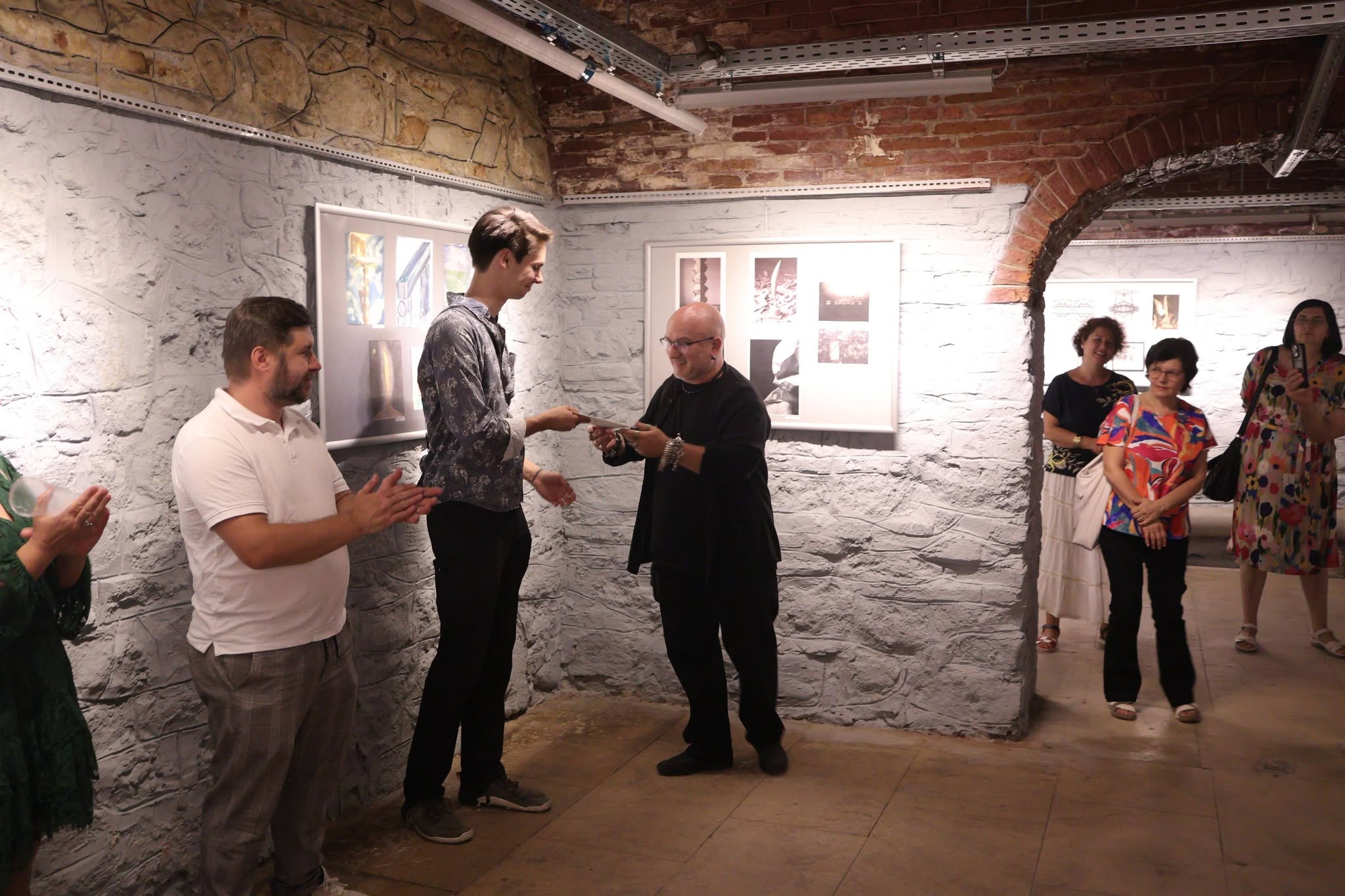 A group of people in front of a group mail art exhibition. one man receives a gift from another.