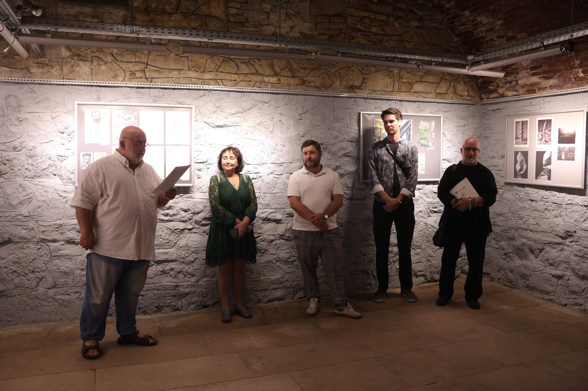 A group of people standing in front of a group art exhibition. one man presents the exhibition.