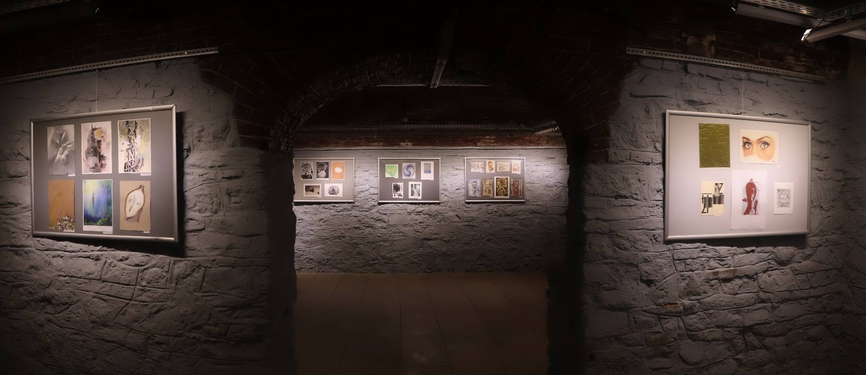 A series of art pieces on walls in an exhibition space. International mail art group exhibition.