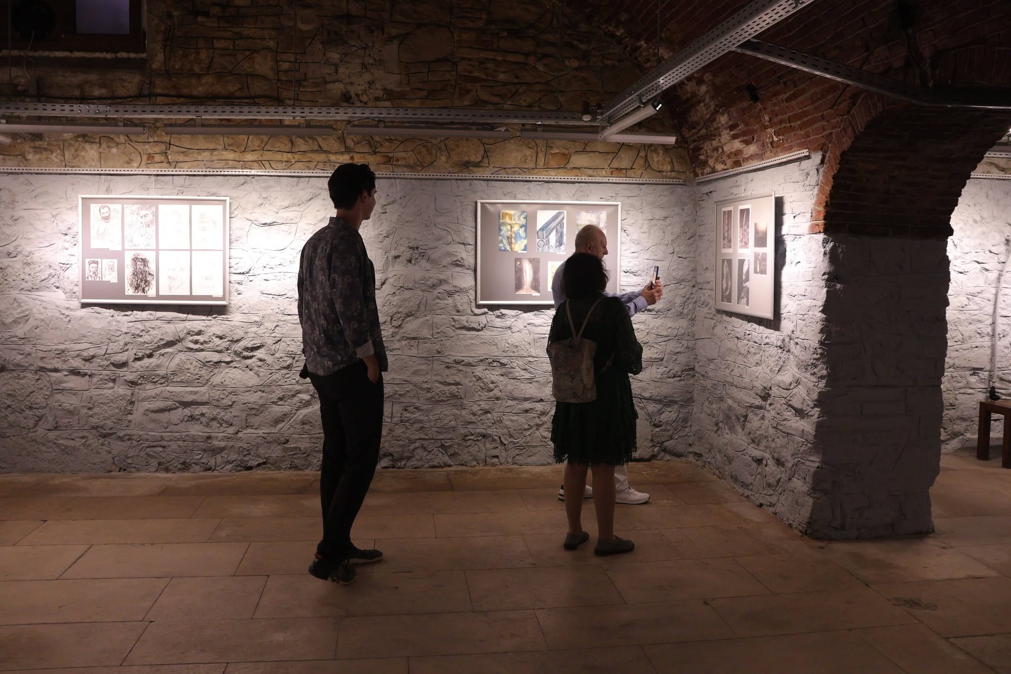Two people look at artwork on the wall at a group mail art exhibition.