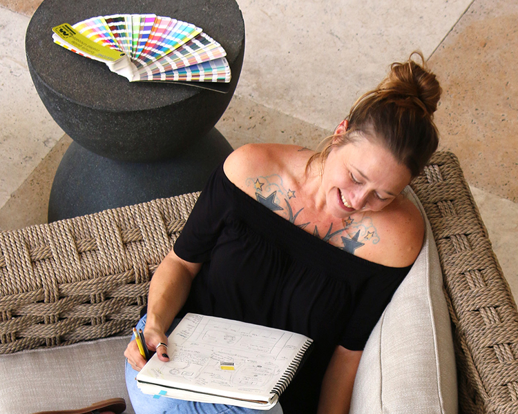 Danni Goodman sketching logo concepts in a notebook with a Pantone color fan nearby.