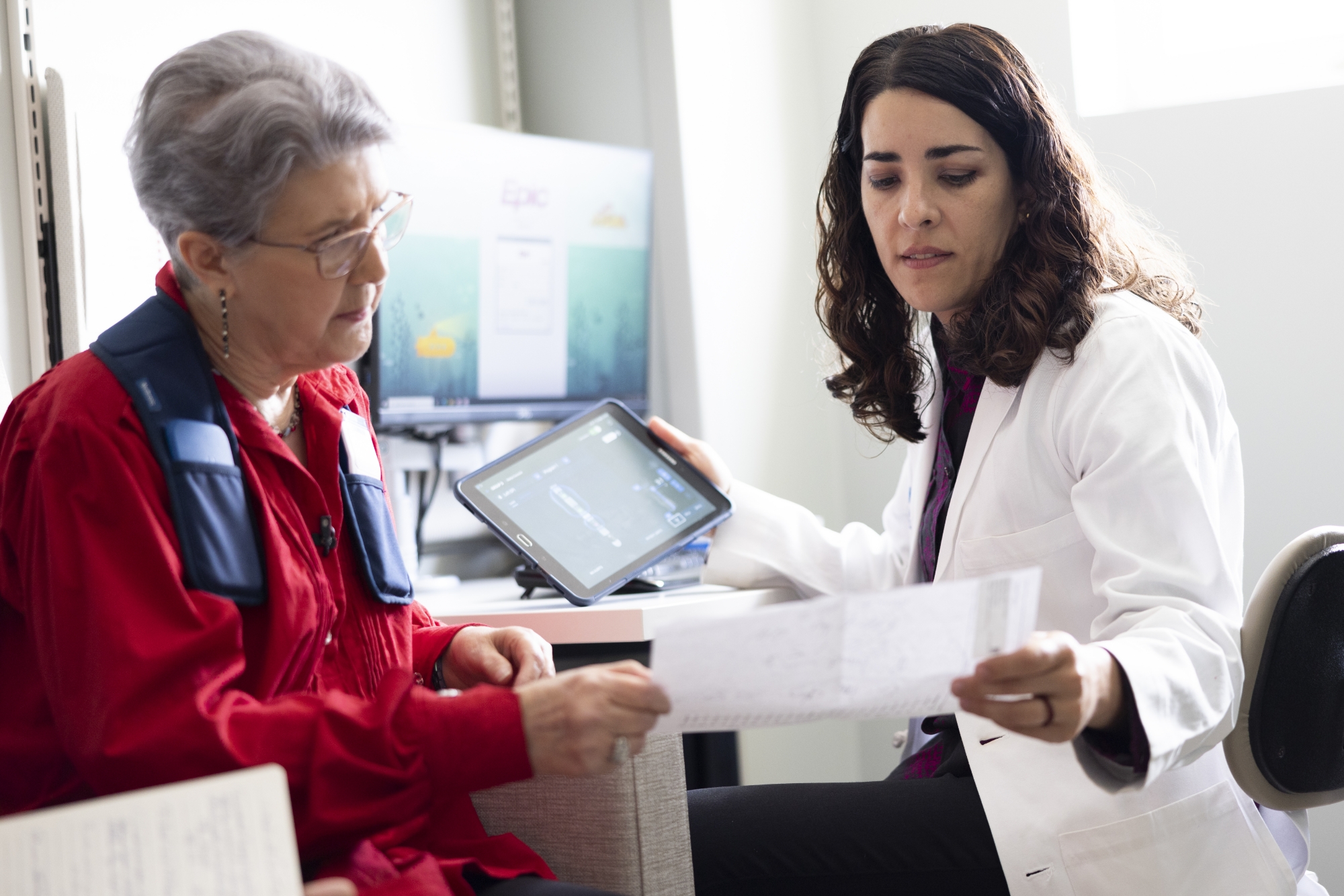Doctor reviewing a document with an older patient while holding a tablet during a consultation.
