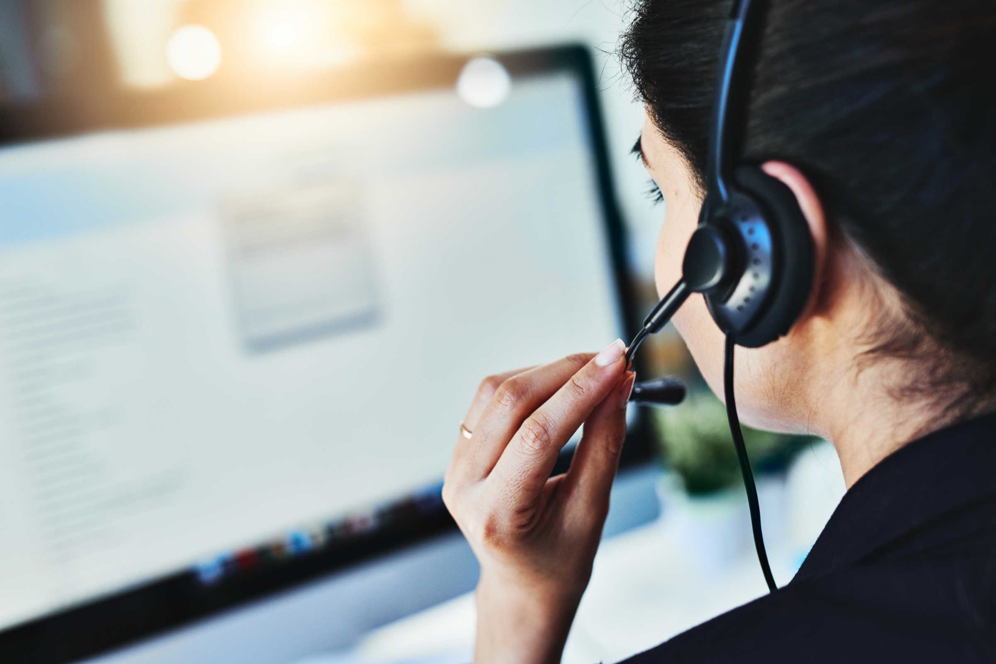 Person wearing a headset and speaking into a microphone while working at a computer, representing telehealth services.