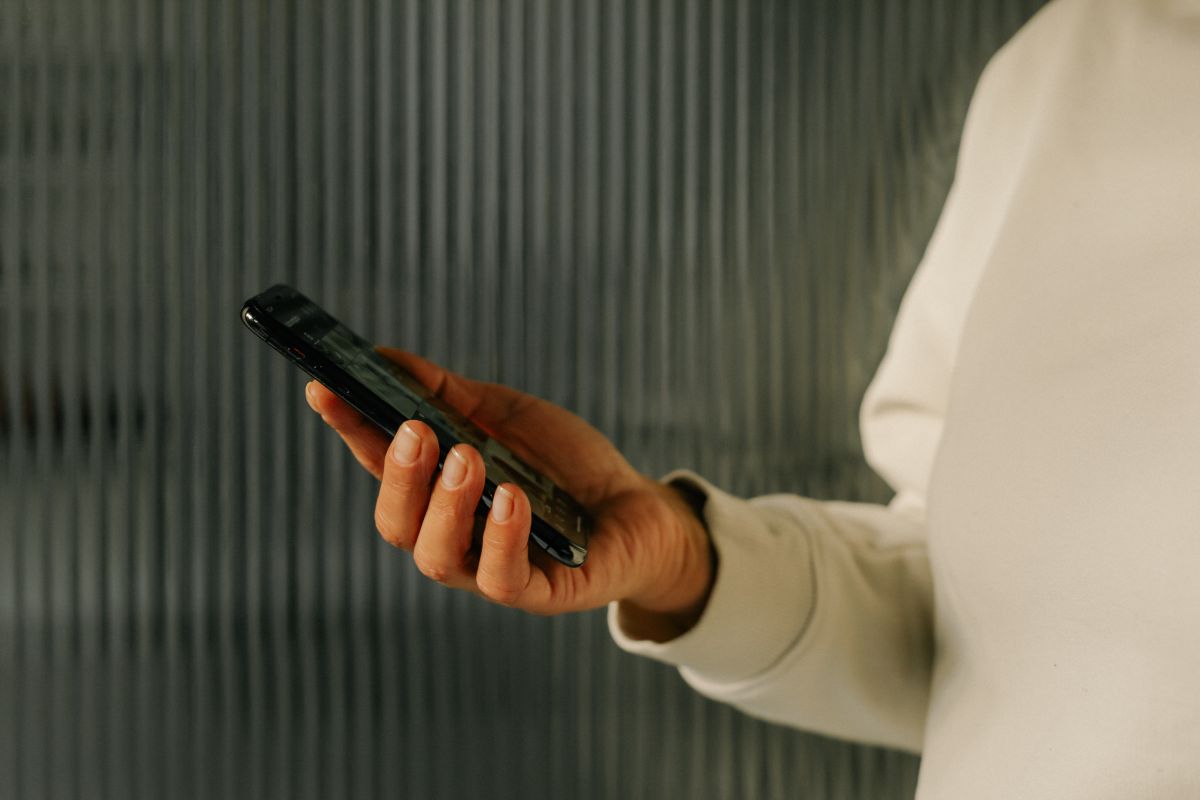Person holding a smartphone in their right hand against a blurred vertical lined background.
