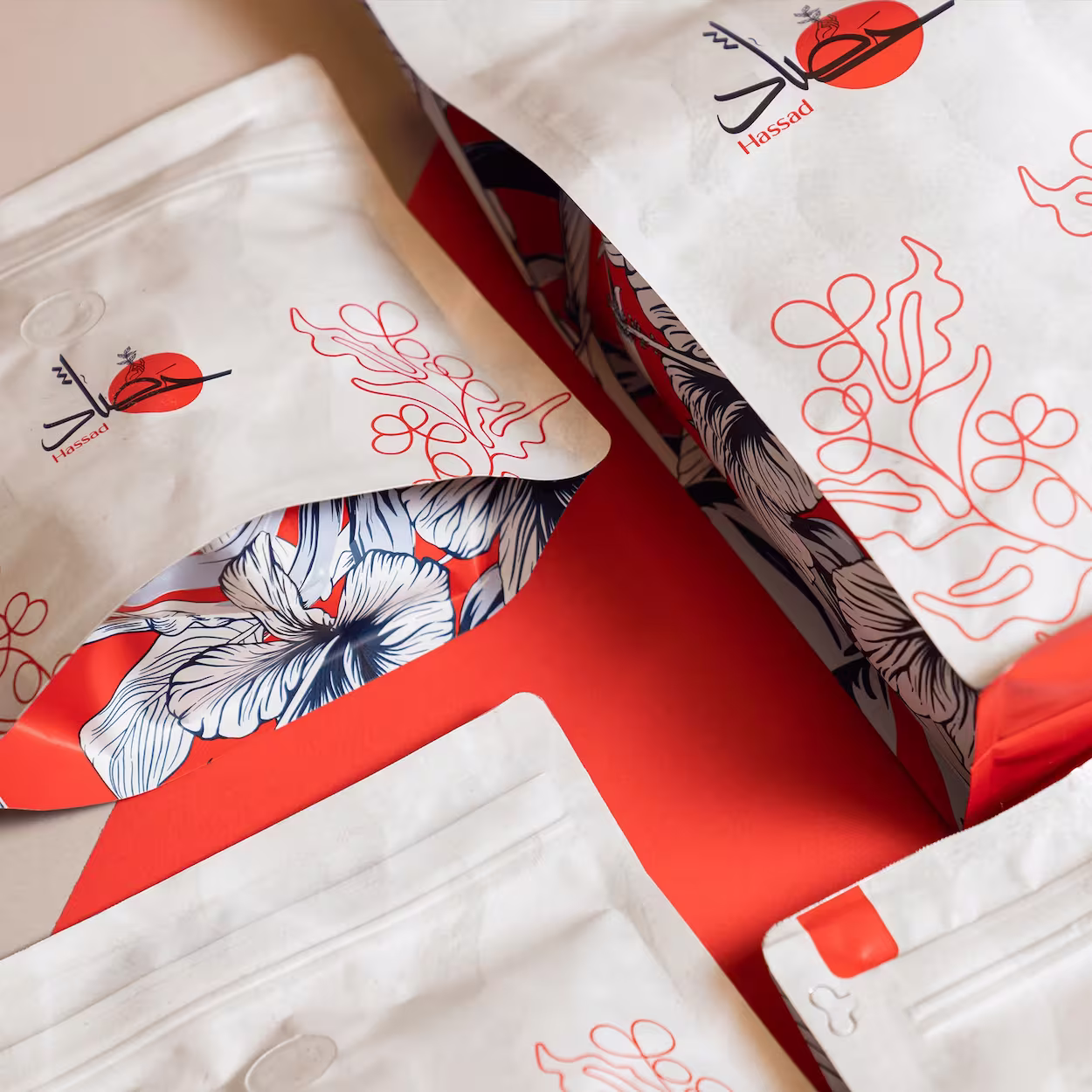 White packaging with black, red botanical designs and 'Hassad' logo on a red surface.