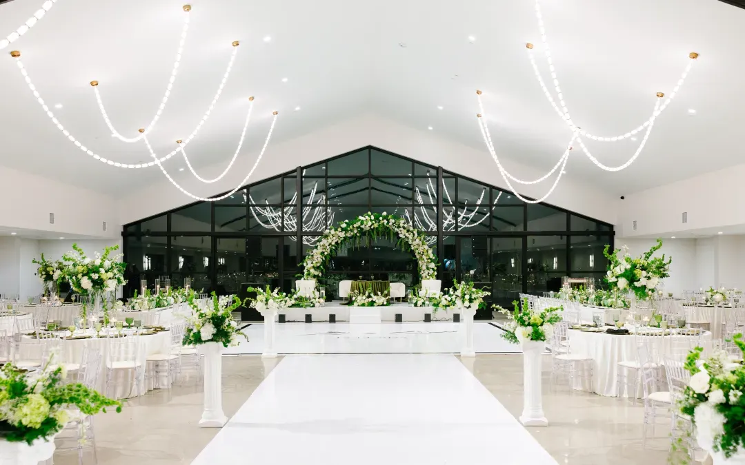 Ballroom set for a reception with a white aisle runner and a floral arch