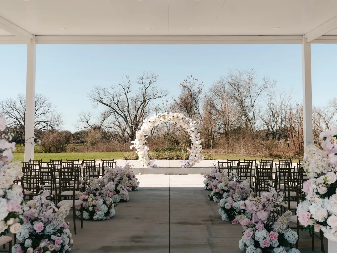 Outdoor ceremony pavilion with a round floral arch and pink and white aisle flowers