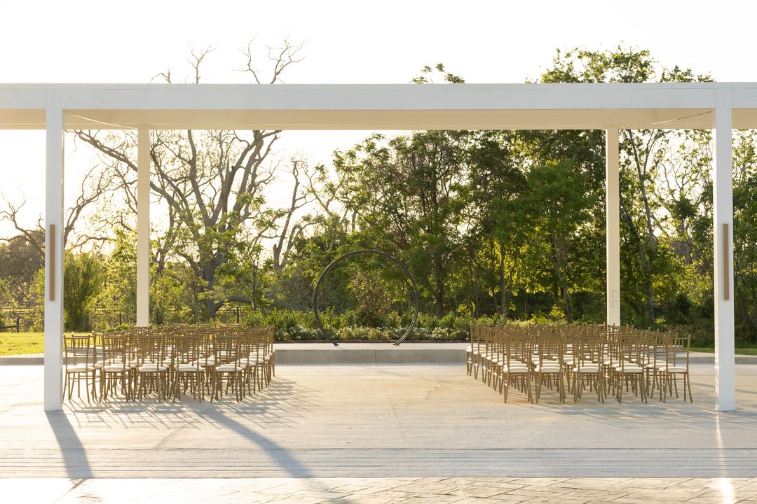 White outdoor ceremony pavilion with rows of wooden chairs