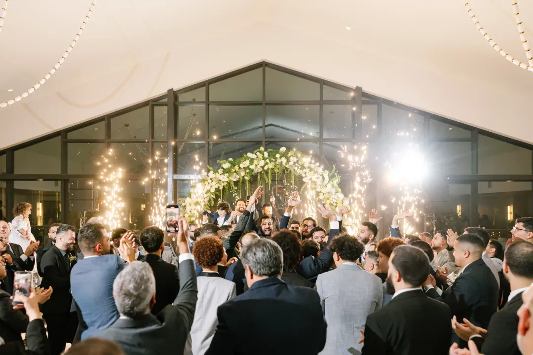 Guests cheering as the couple enters the ballroom under a floral arch