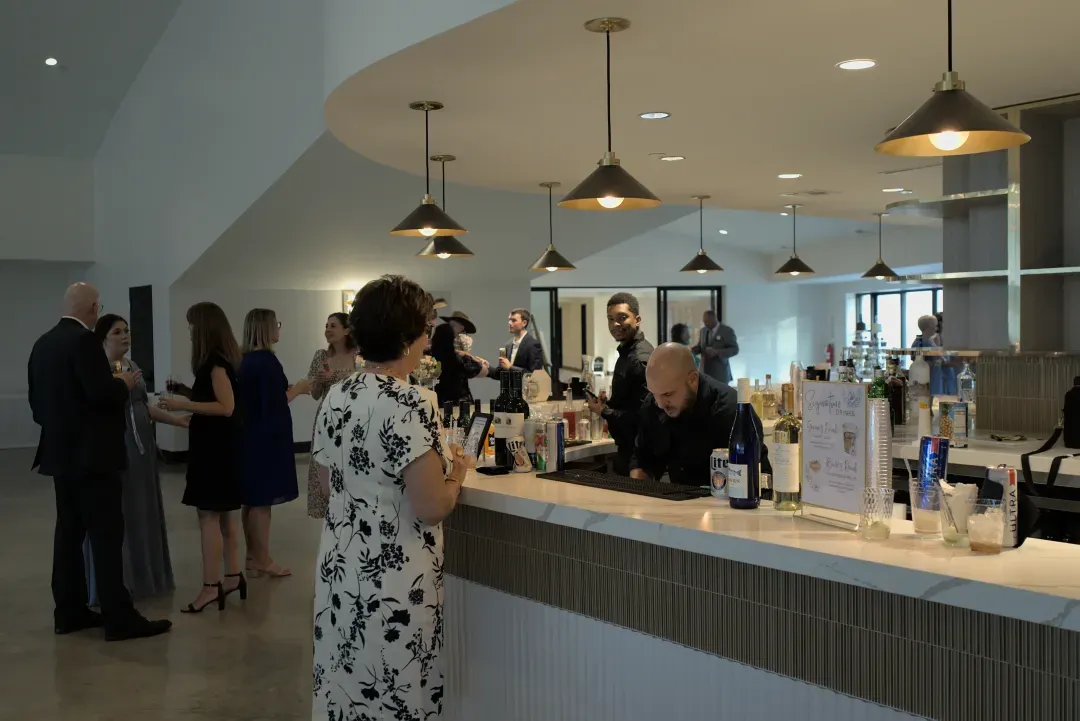 Guests ordering drinks at the curved white bar under pendant lights