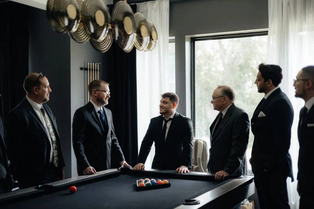 Groom and groomsmen in suits around the pool table in the groom's lounge