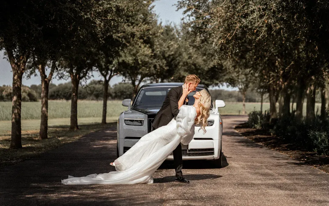 Couple kissing beside a white Rolls-Royce on the oak-lined drive