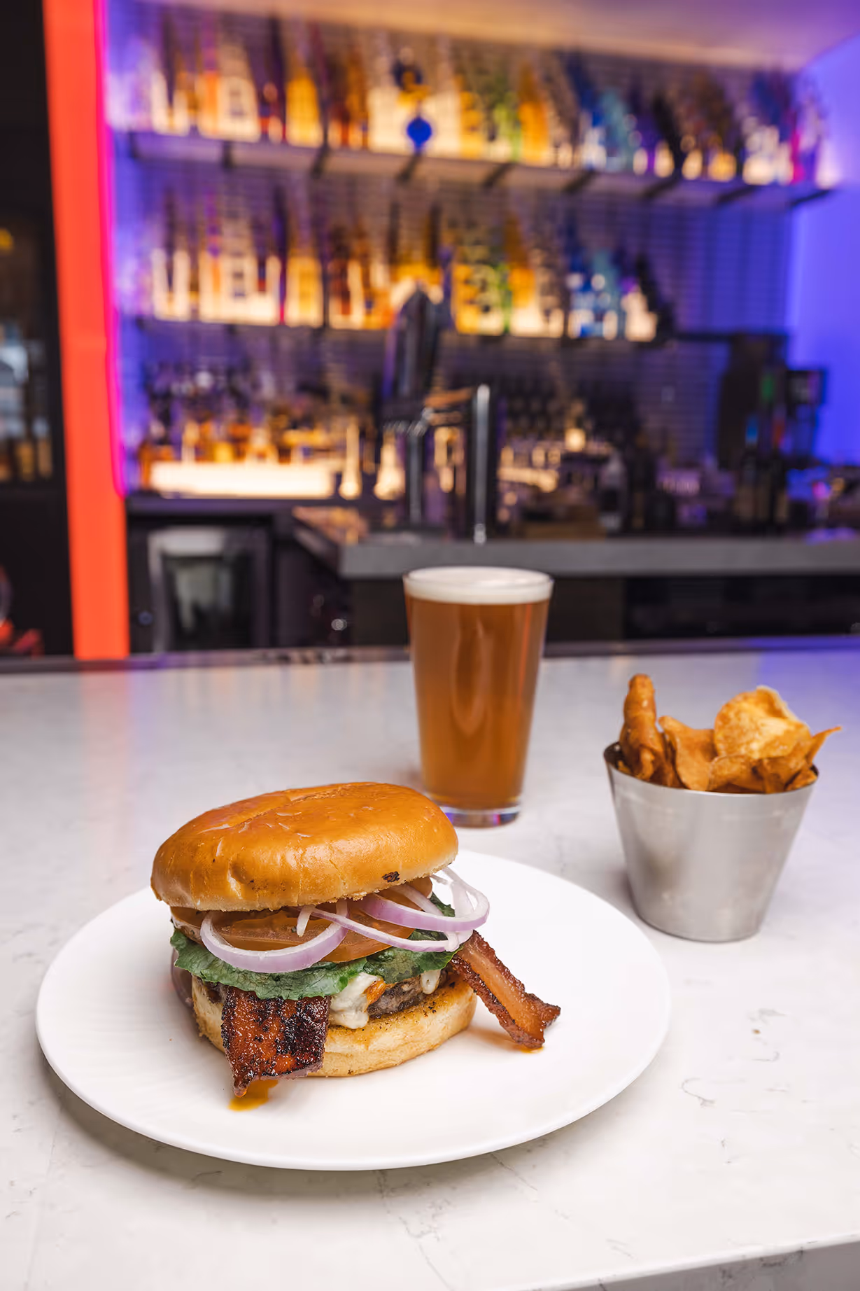 A Candied Bacon Cheeseburger served with chips and a glass of beer