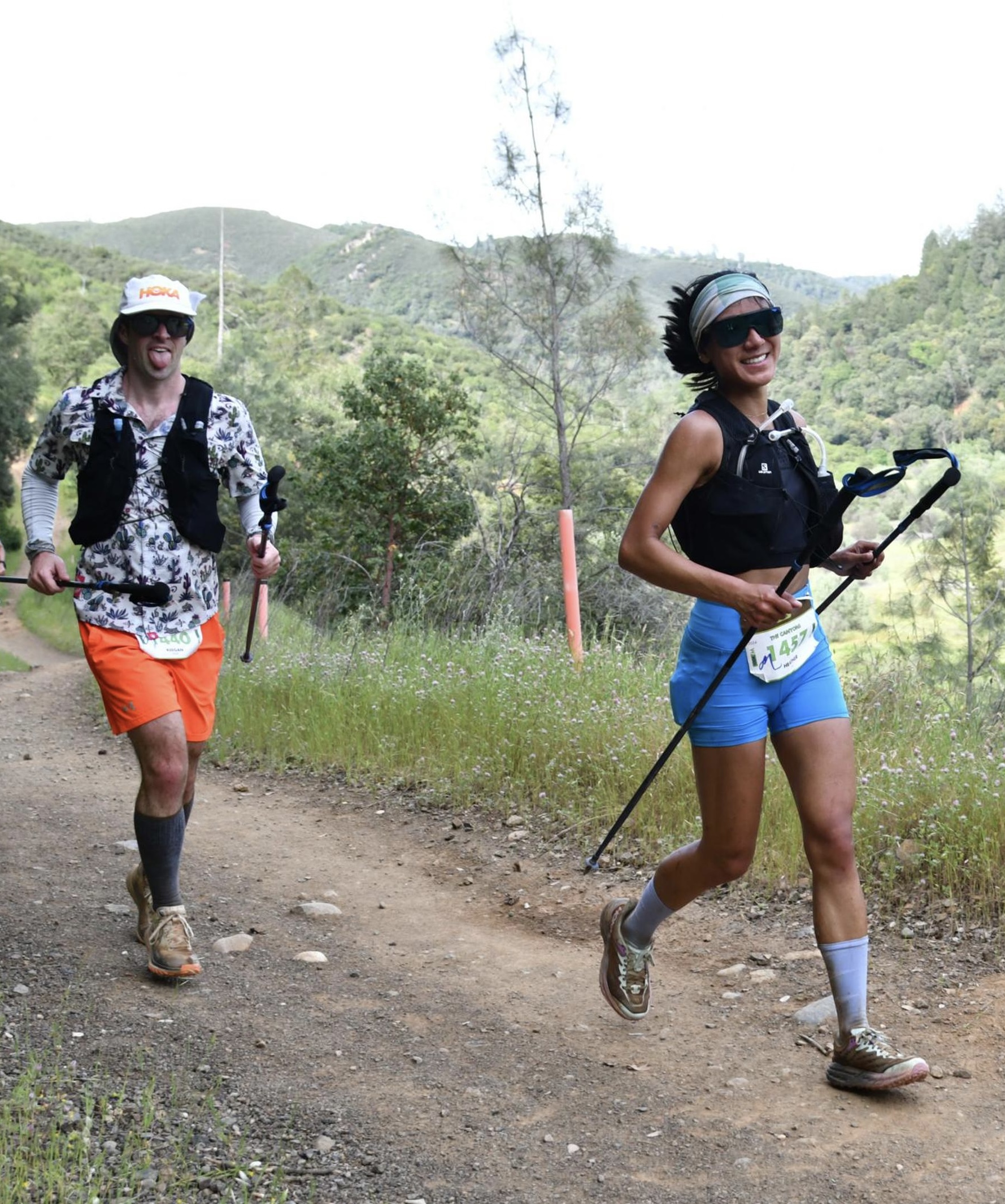 A man and woman are running on a trail with a mountain in the background.