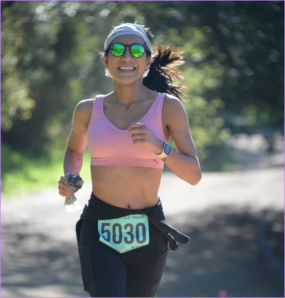 A woman wearing a pink tank top and sunglasses is running.
