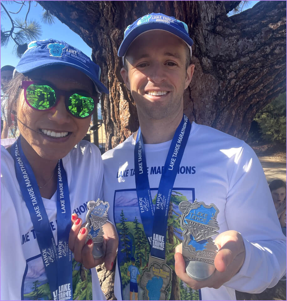 A man and woman are holding medals for the Lake Marathon.