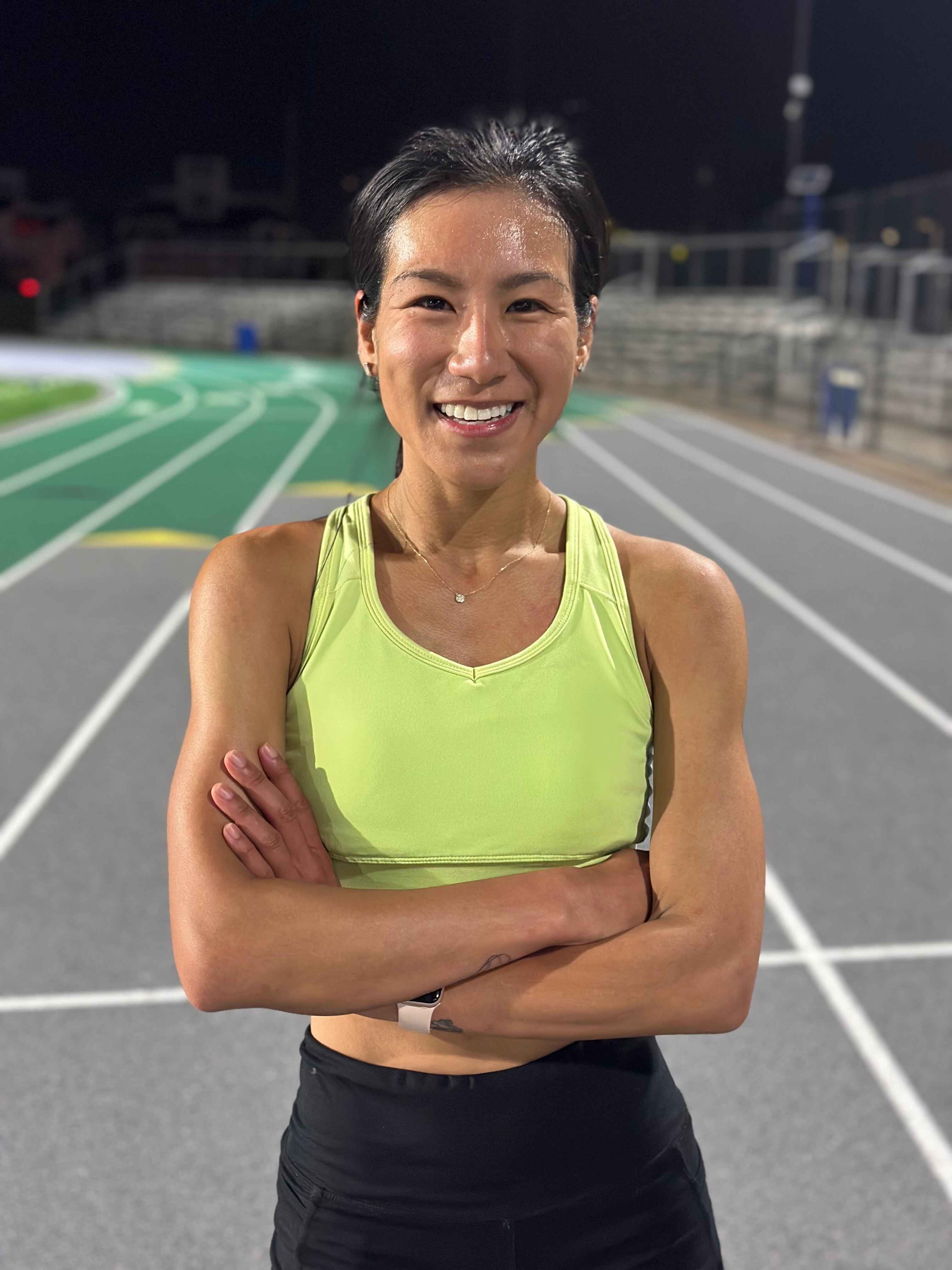 A woman in a yellow tank top posing on a track.