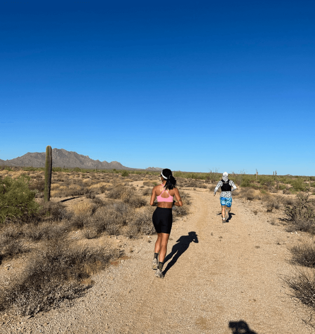 Two women running on a dirt trail in a desert.