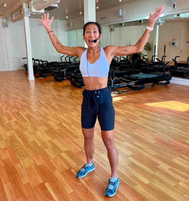 A woman wearing a microphone and shorts is standing in a gym.