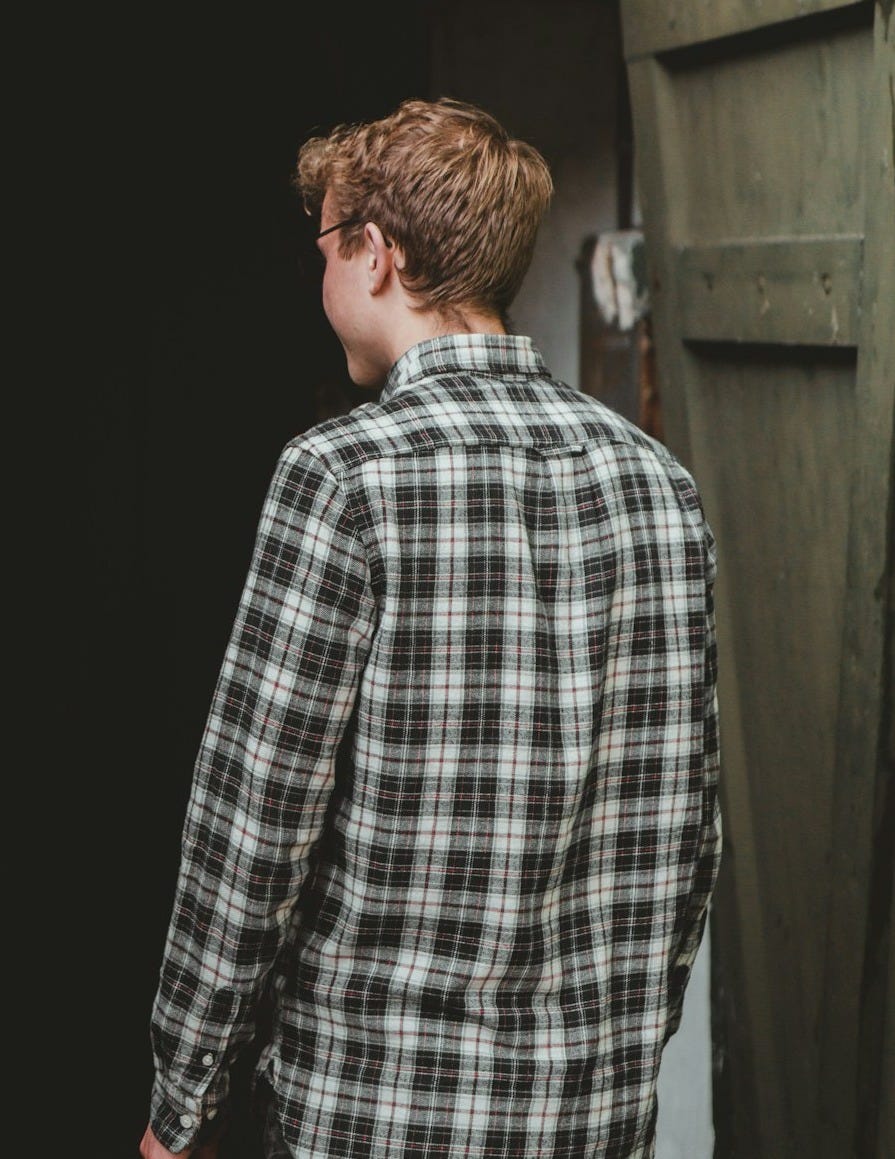 man in black and white plaid dress shirt standing near brown wooden door