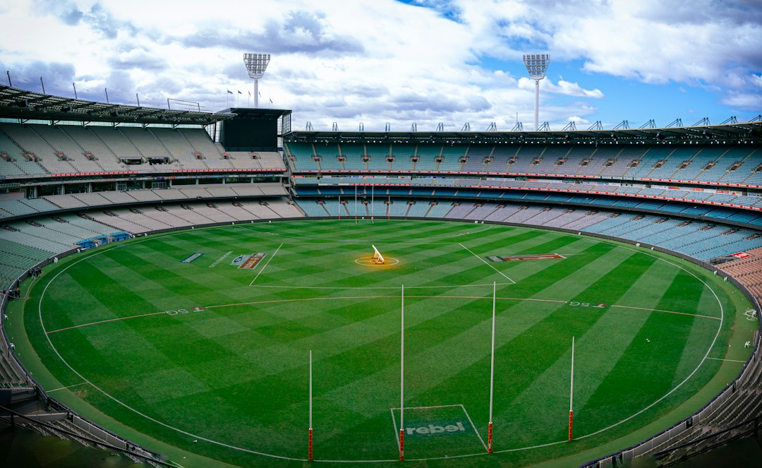 a sports stadium with a field and a field with a crowd of people with Melbourne Cricket Ground in the background