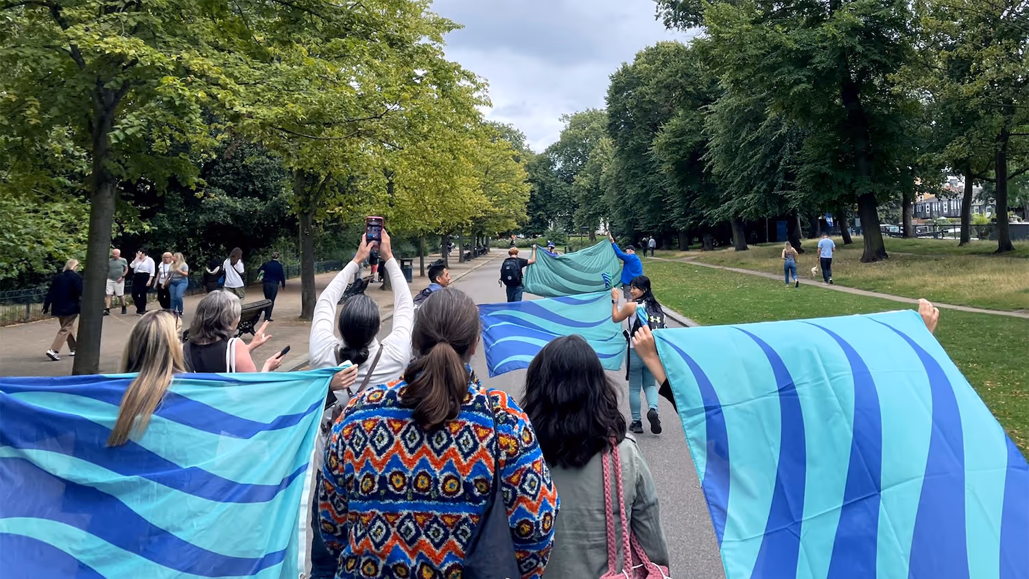 A group of people are walking through a park, waving stammering pride flags.