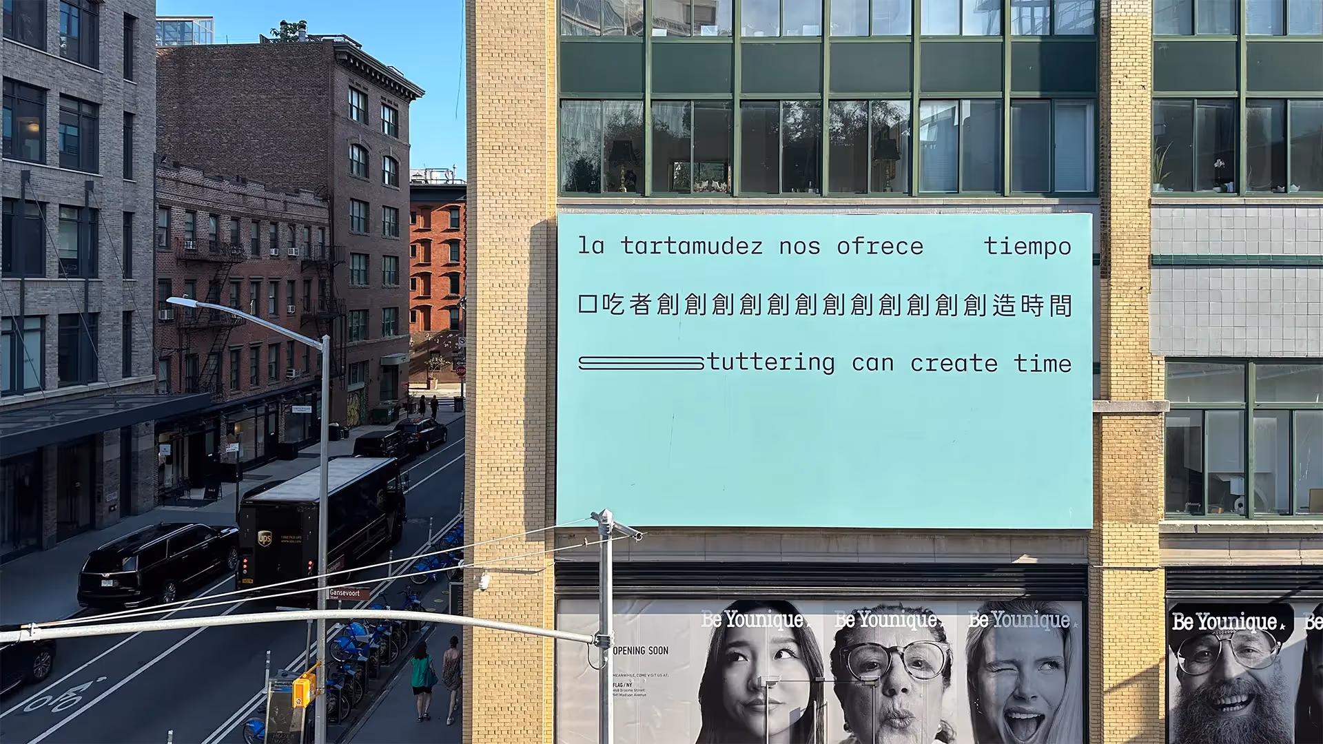 A seagreen billboard on a Manhattan building. It reads ‘stuttering can create time’ in Spanish, Chinese and English.