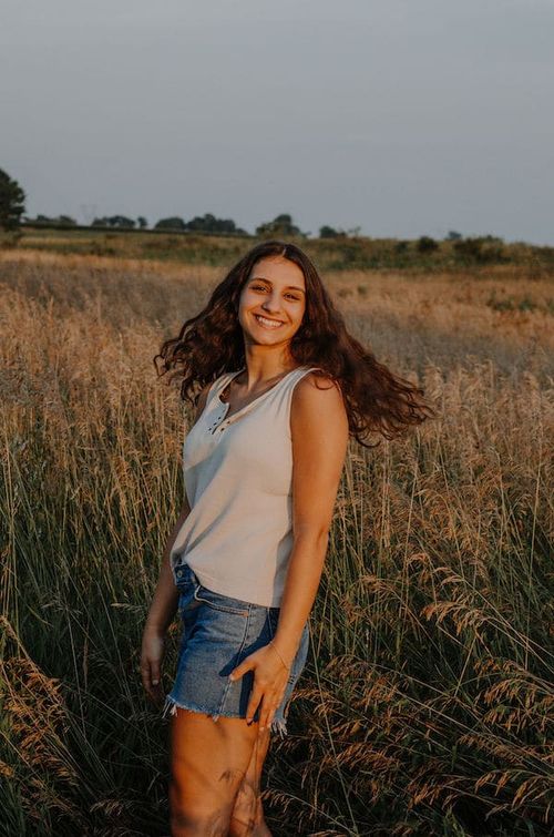 a young woman standing in a field at sunset