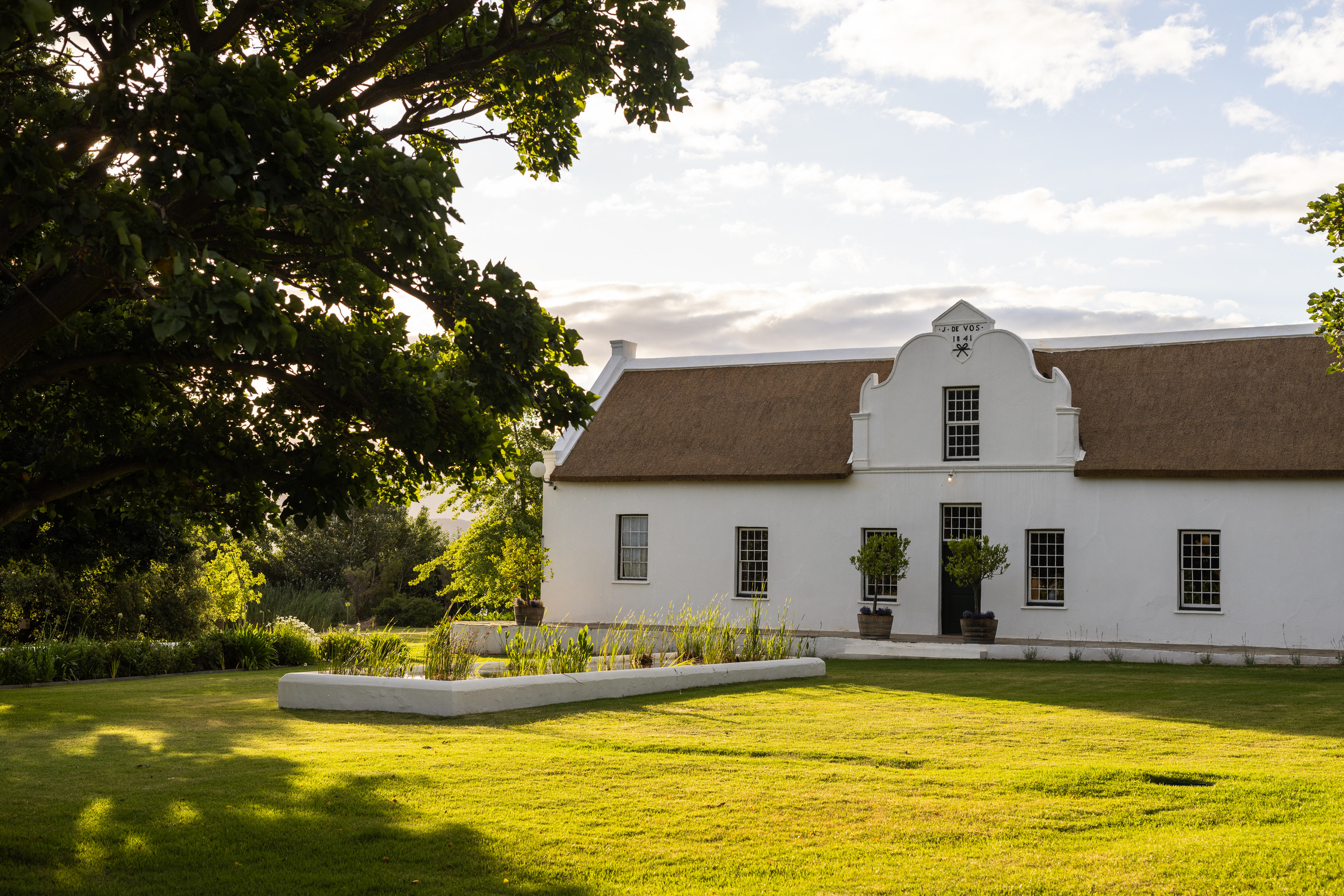 An elegant bedroom glimpsed through a mirror reflection, showcasing a blue-striped bedspread and a ceramic table lamp.