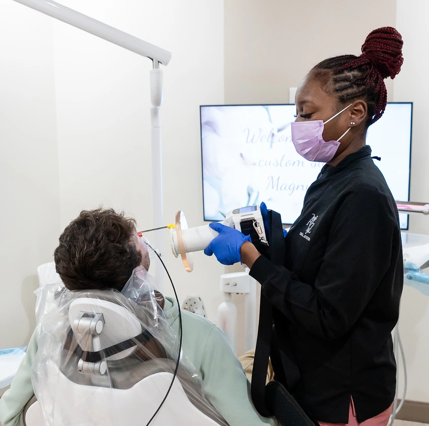 Dental professional wearing mask and gloves uses scanning device on seated patient's teeth for impression.