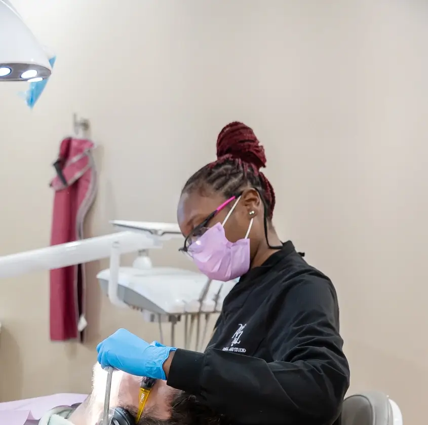 Dentist in gloves and mask treating patient lying back in dental chair under light.
