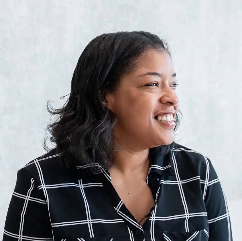Smiling woman with shoulder-length hair wearing a black and white checkered shirt looking right.