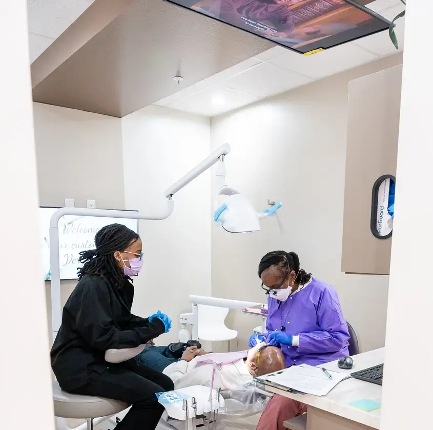 Dentist and assistant wearing masks and gloves treating a patient in a dental clinic.