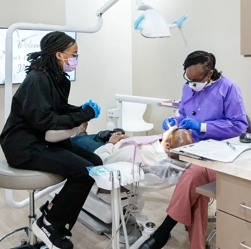Dr. Ashlee Goodman-Tabari treating patient while assistant in black with gloves watches nearby.