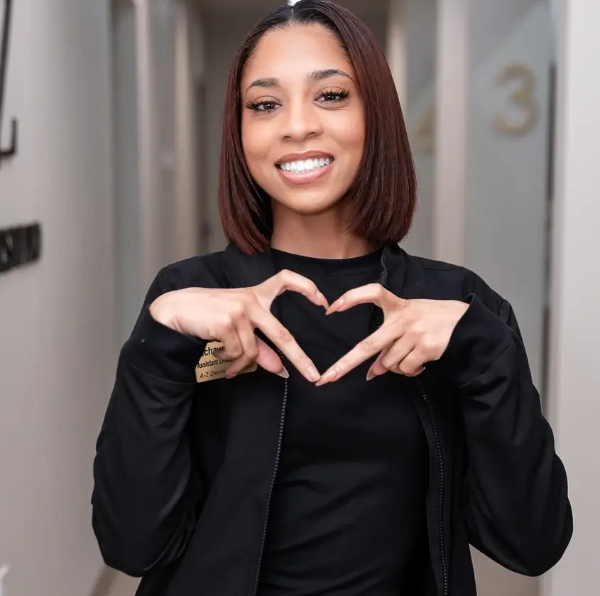 Smiling woman forming a heart shape with her hands wearing a black jacket and shirt.