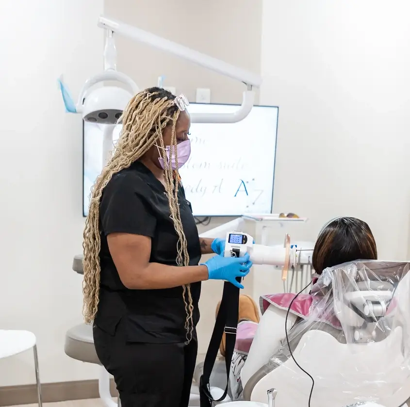Dental professional in black scrubs using a handheld device on a patient seated in a dental chair.