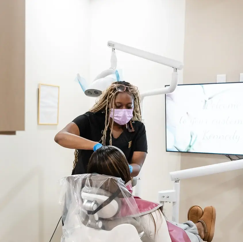 Dentist wearing mask and gloves treating a patient reclined in a dental chair in a clinic.
