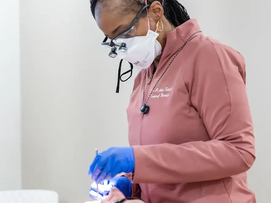 Female dentist wearing mask and magnifying glasses while treating a patient.